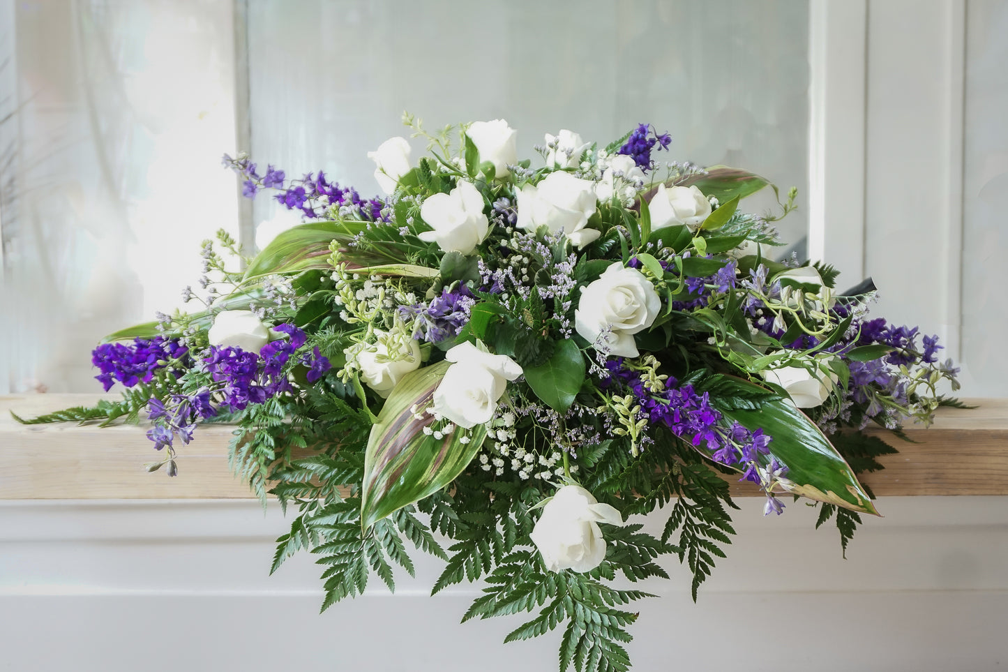 jolie coussin composé de delphiniums mauves et roses blanches ainsi que du delphiniums mauves